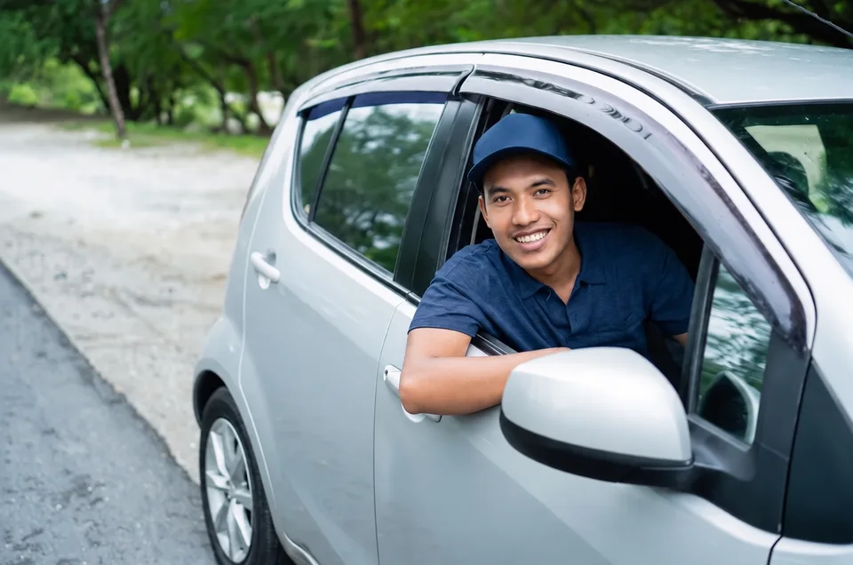 A smiling driver at the open window of a silver car.